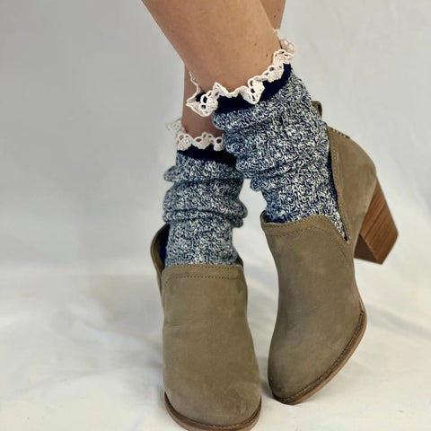 A close-up of legs wearing Catherine Cole MARLED Cotton Short Lace Boot Socks in Navy, featuring white lace trim, scrunched above tan suede heeled ankle boots, set against a white background.