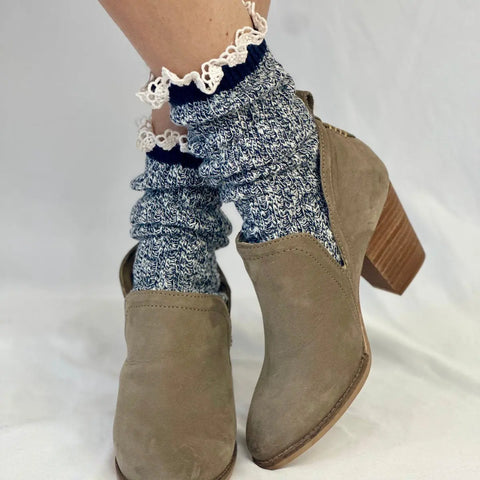 A person wearing tan heeled ankle boots and Catherine Cole MARLED Cotton Short Lace Boot Socks in Navy stands on a white background.