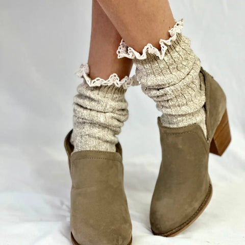 A person wearing light brown ankle boots and Catherine Cole MARLED Cotton Short Lace Boot Socks in tan, featuring white ruffled trim, stands against a plain white background.