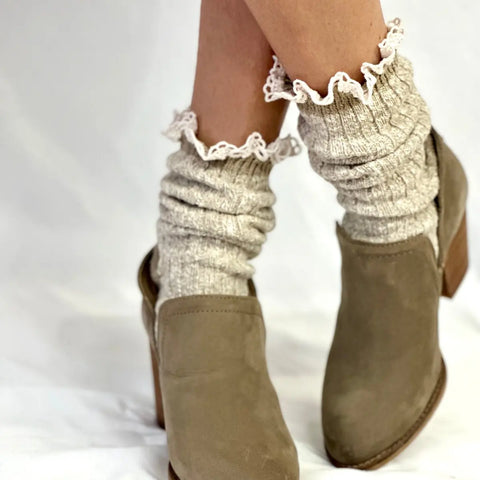 Close-up of a person wearing Catherine Cole’s MARLED Cotton Short Lace Boot Socks in Tan—thick, light gray knit with a ruffled trim—paired with beige heeled shoes, standing on a white surface.