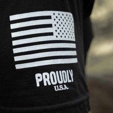 A close-up of the Proudly Star Mens Cotton T-Shirt by Proudly USA, a black tee featuring a white American flag graphic above PROUDLY U.S.A. and made in the USA.