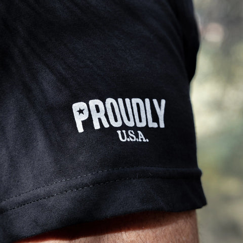 Close-up of the Proudly USA American Flag Mens Cotton T-Shirt (Black), featuring a black sleeve with PROUDLY and U.S.A. printed in white and a star inside the O—ideal for those seeking a patriotic tee made in the USA.