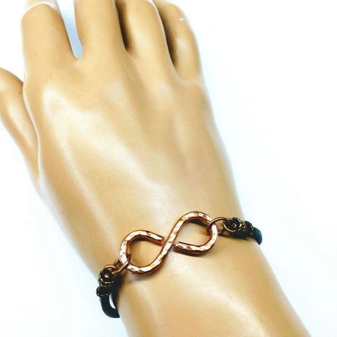 A hand wears the Masculine Sturdy Copper Swivel Infinity Bracelet by Alexa Martha Designs, featuring a metallic infinity centerpiece on a sleek black band.