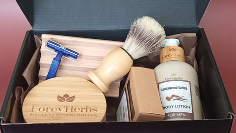 The Men's Grooming Gift Set by Forev'Herbs includes a blue razor, shaving brush, round wooden box, Cedarwood Shaving Cream, Natural Handmade Soap, and sandalwood vanilla body lotion in a black gift box—an ideal men's care gift.