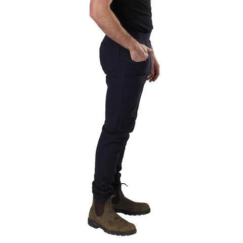 A man in profile wears a black t-shirt, Spiritex Saratoga Pants (organic cotton, slim-fit) and brown suede boots, one hand in his pocket, standing against a white background.