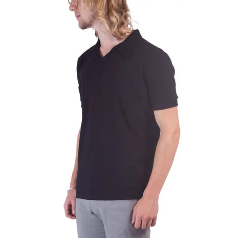 A person with long blond hair and glasses wears the Spiritex Short Sleeve Mt. Mitchell Collared Shirt in black organic cotton and gray pants, standing sideways against a white background.