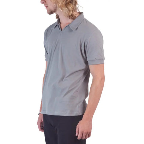 A person with long, wavy blond hair wears the Spiritex Short Sleeve Mt. Mitchell Collared Shirt in light gray and black pants, standing sideways against a white background.