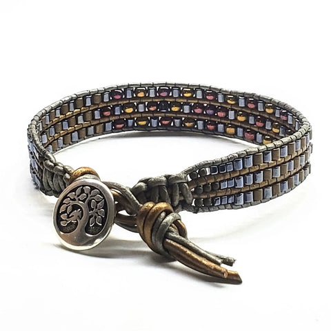 The Mens Tree of Life Intricately Beaded Leather Wrap Bracelet by Alexa Martha Designs features earth-tone square beads and a leather cord with a Tree of Life button closure, shown on a white background.