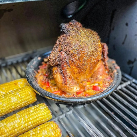 A whole chicken seasoned with Gustus Vitaes Mexican Seasoning Gift Set roasts upright with veggies on the grill, next to charred corn.