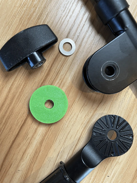 Alpaca Mics Mic Stand Saver includes assorted black metal and plastic chair adjustment parts, plus green and silver washers, all compatible with mic boom stand setups and displayed on a wooden surface.