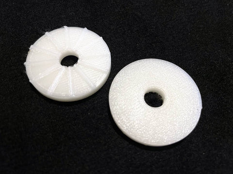 Two white, round plastic Mic Stand Saver discs by Alpaca Mic are placed on a black surface. The left disc has segmented lines, while the right is smoother. Both can serve as rubber washers for a mic boom stand.