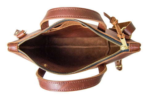 A top-down view of an open Quinn Crossbody by Urban Southern, featuring a gold zipper and two handles, crafted from premium leather, with its empty interior visible against a white background.