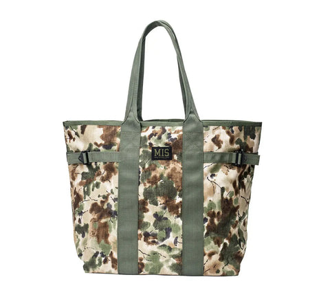 The MIS Multi Tote Bag - Covert Woodland features a camouflage pattern, green handles and vertical straps, a black and gold MIS logo patch on the front, is water-resistant, and made in the U.S.A.