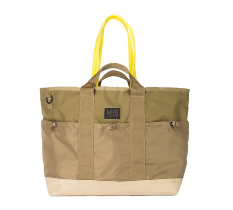 The MIS Multi Pocket Tote Bag - Coyote Tan is crafted from durable Cordura nylon in tan and olive green, with a beige bottom, yellow straps, short tan handles, exterior pockets, and a black MIS patch. Proudly made in the USA.
