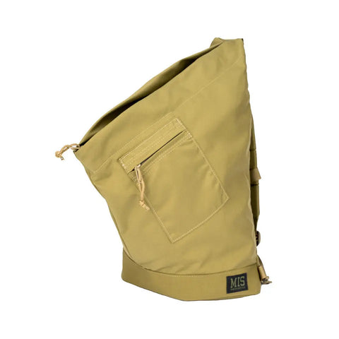 The MIS TA One Shoulder Bag in Coyote Tan is made in the USA from canvas, featuring a front zip pocket, side straps, black MIS patch near the bottom, and a slouchy asymmetrical shape with a drawstring top closure.