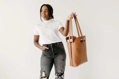 A woman in a white t-shirt and ripped black jeans holds the Urban Southern Mini Market Tote, standing against a plain white background.