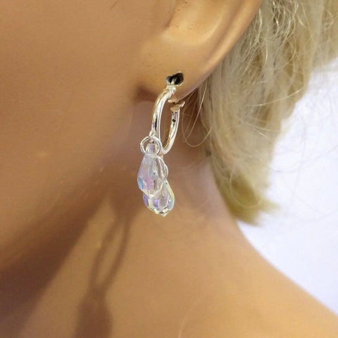 A close-up shows an ear wearing Alexa Martha Designs Sterling Silver Hoop Sparkly Crystal Drop Dangle Earrings, with a faceted clear crystal pendant that shines against a softly blurred background.