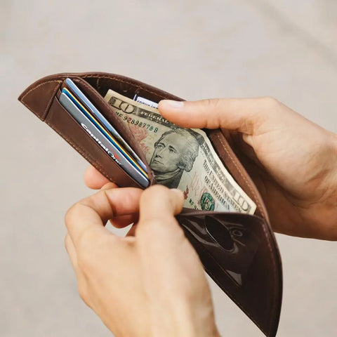 A person holds an open Rogue Industries Rogue Front Pocket Wallet - Classic Made in Maine Edition, showing several credit cards and a visible ten-dollar bill.