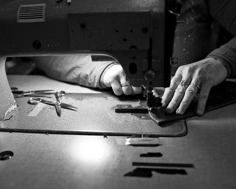 A person crafts a Rogue Industries Rogue Front Pocket Wallet – Classic Made in Maine Edition, guiding premium leather under an industrial sewing machine. In black and white, the image highlights their skilled hands and the machine at work.
