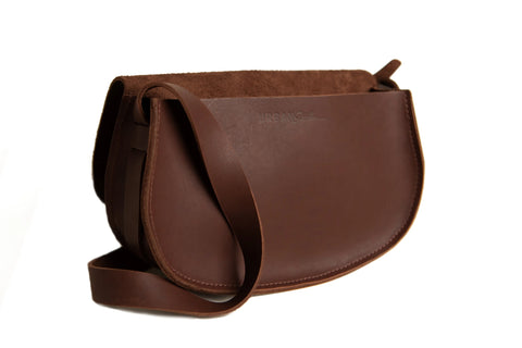 The Urban Southern Half Moon Crossbody, crafted from brown full-grain leather, features a curved flap, long strap, and suede-lined interior. Shown on a white background.