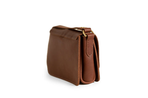 The Urban Southern Lancaster 5-Pocket Crossbody is a small brown full-grain leather bag with gold-tone hardware. Shown from the side on a white background, its structured shape highlights minimalist style and understated design.