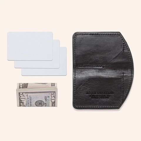 The Minimalist Wallet by Rogue Industries, shown in black, lies open beside three blank cards and a folded stack of U.S. fifty-dollar bills, all neatly arranged on a light beige background.