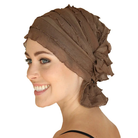 A smiling woman with light skin and green eyes models the Chemo Beanies® Sara textured brown chemo beanie, viewed from the side against a plain white background.