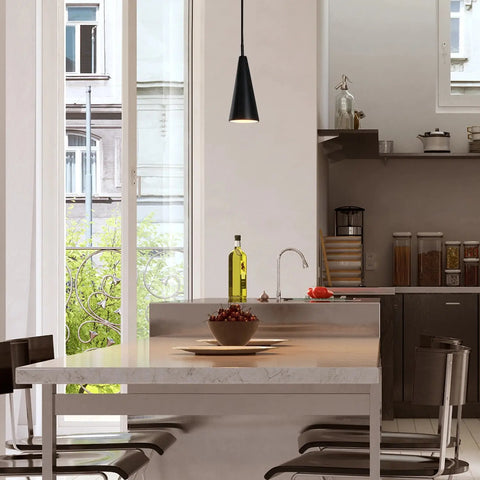 Modern kitchen featuring a marble island, four dark chairs, and a large window. The Fossil Mini Pendant by A19 Artisan Lighting, handcrafted in California, brings modern elegance above the counter decorated with olive oil and apples.