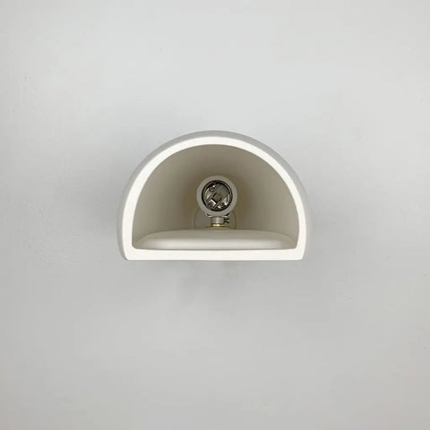 The Aruba Sconce by A19 Artisan Lighting is a white, semi-circular modern wall light from their USA-made collection, handcrafted in California and featuring a visible light bulb mounted on a plain white wall.