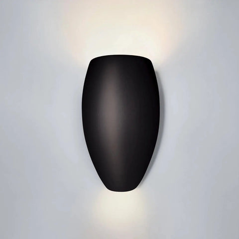 The Modern USA-Made Aruba Sconce by A19 Artisan Lighting features a smooth, curved black design that casts soft up and down lighting against a white wall; handcrafted in California.