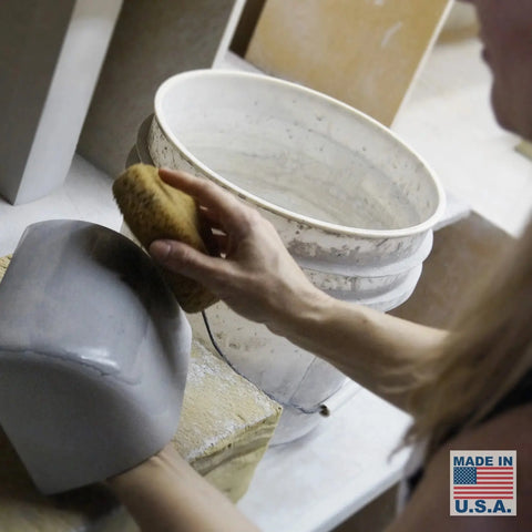 A person smooths a gray ceramic piece near a white bucket while a Made in U.S.A. label highlights the handcrafted Balboa Downlight Sconce by A19 Artisan Lighting, perfect for pairing with LED smart bulbs.