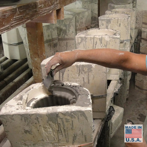 In a pottery workshop, someone pours clay slip into a ceramic mold. On a shelf nearby are several molds, a Made in U.S.A. label, and an A19 Artisan Lighting Modern Bamboo Sconce, handcrafted in California.