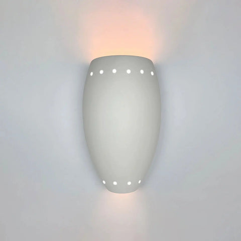 A white ceramic Barbados sconce with perforated holes on the surface, mounted on a wall and projecting light patterns.