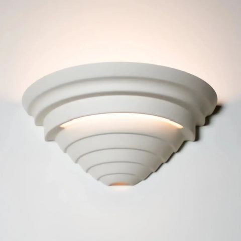 The Cabrera Sconce by A19 Artisan Lighting is a modern, handcrafted wall light made in California, featuring a layered geometric design that casts an ambient glow both upward and downward on white walls.