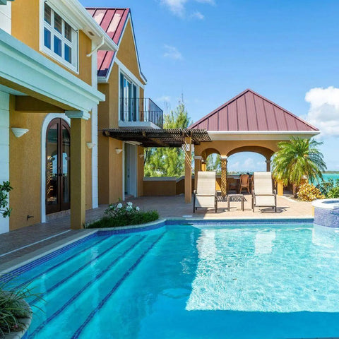 A luxurious house with a poolside patio, tropical plants, and ocean views is elegantly lit by the Modern USA-Made Wall Lighting – Cabrera Sconce, handcrafted in California by A19 Artisan Lighting.