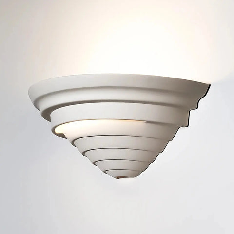 The Cabrera Sconce by A19 Artisan Lighting is a modern, white, cone-shaped wall light with stepped ridges, handcrafted in California. Made in the USA, it emits soft upward light for a subtle wall glow.