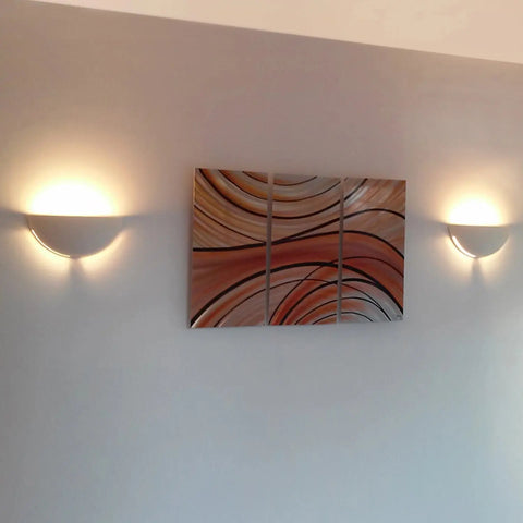 A modern wall features two A19 Artisan Lighting Capri Sconces, handcrafted in California, flanking a six-panel abstract art with brown and beige curves. The LED-lit USA-made sconces cast a soft glow on the light gray wall.
