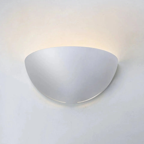 The Modern USA-Made Capri Sconce by A19 Artisan Lighting, handcrafted in California, features a sleek semi-circular white design that emits soft upward light, creating a gentle glow on any plain white wall.