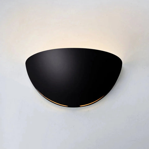 The Modern USA-Made Capri Sconce by A19 Artisan Lighting, handcrafted in California, casts a soft, warm glow upward on a white wall, blending contemporary design with understated elegance.