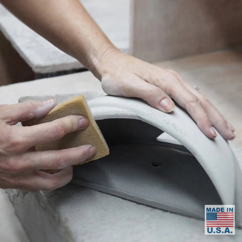 An artisan smooths a curved ceramic piece for the Modern USA-Made Wall Lighting – Ceylon Sconce by A19 Artisan Lighting, handcrafted in California. A Made in USA label with an American flag appears in the lower right corner.
