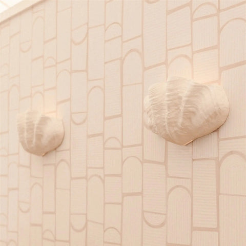 Two Fiji Sconces by A19 Artisan Lighting emit soft light against a beige patterned wall. Handcrafted in California, these modern USA-made wall lights add a minimal, coastal feel to any space.