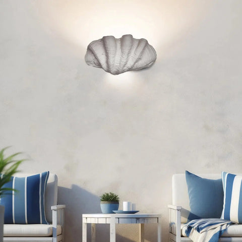 The Modern USA-Made Fiji Sconce by A19 Artisan Lighting, handcrafted in California, brightens a cozy sitting area with two white armchairs with blue cushions, a table and potted plant, and minimal beach-inspired decor.