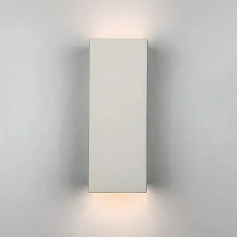 A19 Artisan Lighting’s Modern USA-Made Flores Sconce, handcrafted in California, is mounted on a light gray wall and emits a soft glow above and below with LED smart bulbs.