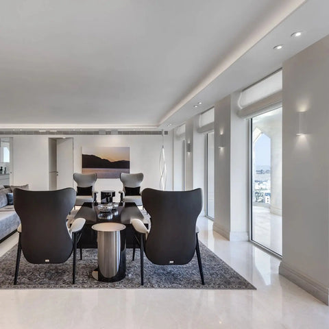 Modern living room with four black accent chairs and a coffee table, highlighted by the Flores Sconce from A19 Artisan Lighting—USA-made wall lighting handcrafted in California—complementing minimalist décor and floor-to-ceiling windows.