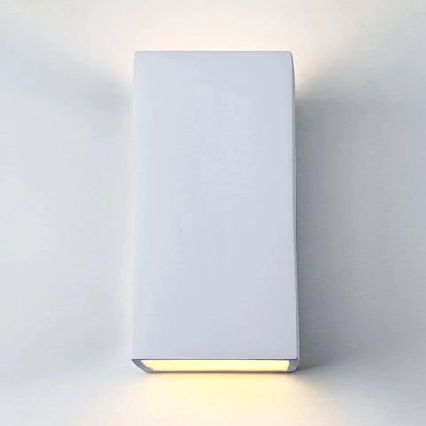 The Modern USA-Made Flores Sconce by A19 Artisan Lighting, handcrafted in California, is a sleek rectangular white fixture casting soft up and down light on a white wall—compatible with LED smart bulbs for convenience.