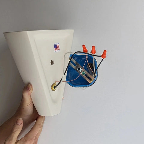 A person holds the Modern USA-Made Wall Lighting – Gotlandia Sconce by A19 Artisan Lighting near a wall, with visible wire nuts and blue electrical box, ready to install energy-efficient LED bulbs. Handcrafted in California.