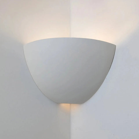A gray ceramic corner sconce mounted on a wall, emitting light from the top and bottom openings.