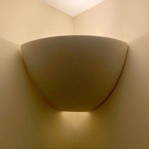 The Gran Aegina Corner Sconce by A19 Artisan Lighting is a modern, handcrafted USA-made wall fixture that casts warm up-and-down light where two beige walls meet.