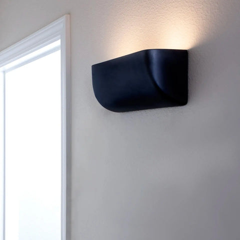 The Gran Balboa Downlight Sconce by A19 Artisan Lighting, handcrafted in California, is a modern black wall light made in the USA that emits soft upward light against a light wall near a bright doorway.