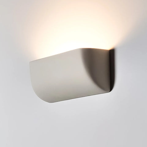 The Gran Balboa Sconce by A19 Artisan Lighting is a modern, USA-made wall light handcrafted in California that emits soft, upward LED illumination and subtle shadows against a white wall.